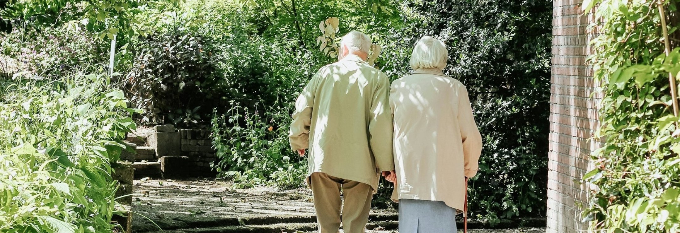 Two older adults walking on a path among greenery